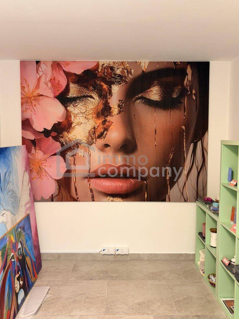 Heller Raum mit großer, auffälliger Kunst an der Wand und Regalen, möglicherweise ein Atelier oder Büro.