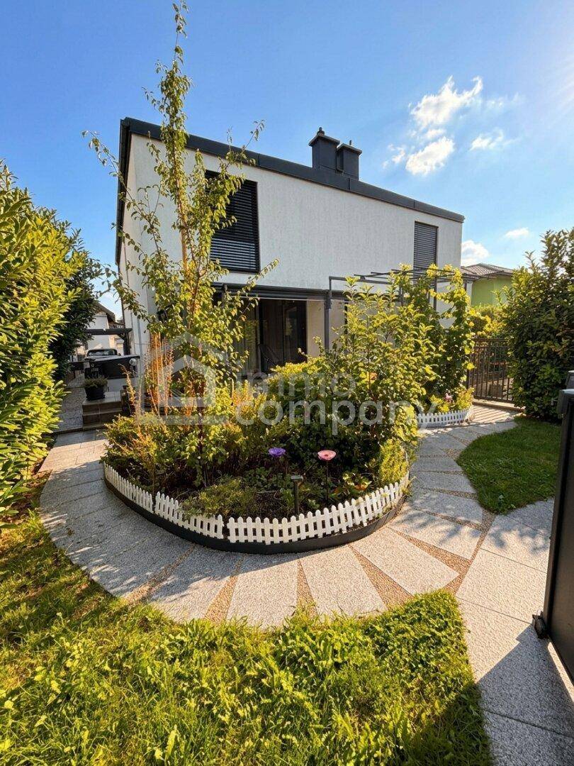 Seitlicher Blick auf das moderne Haus mit geschwungenem Gartenweg und dekorativen Pflanzenbeeten.