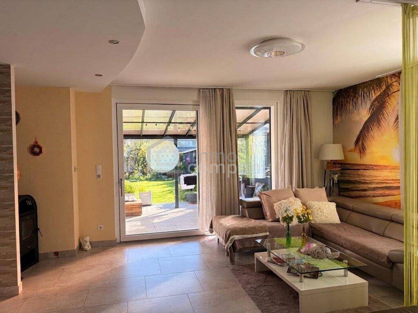 Helles Wohnzimmer mit Fliesenboden, gemütlicher Sitzecke und direktem Zugang zur überdachten Terrasse.
