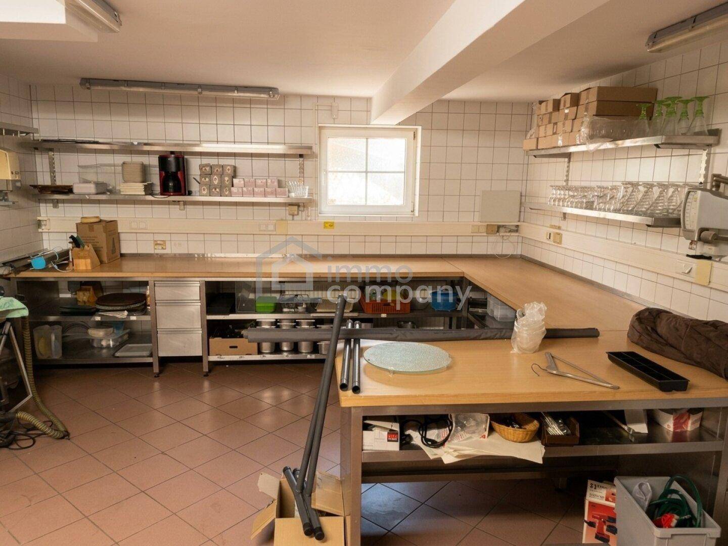 Große Gewerbeküche mit Edelstahl-Arbeitsflächen, Regalen und weißen Fliesenwänden, ideal für Gastronomie.