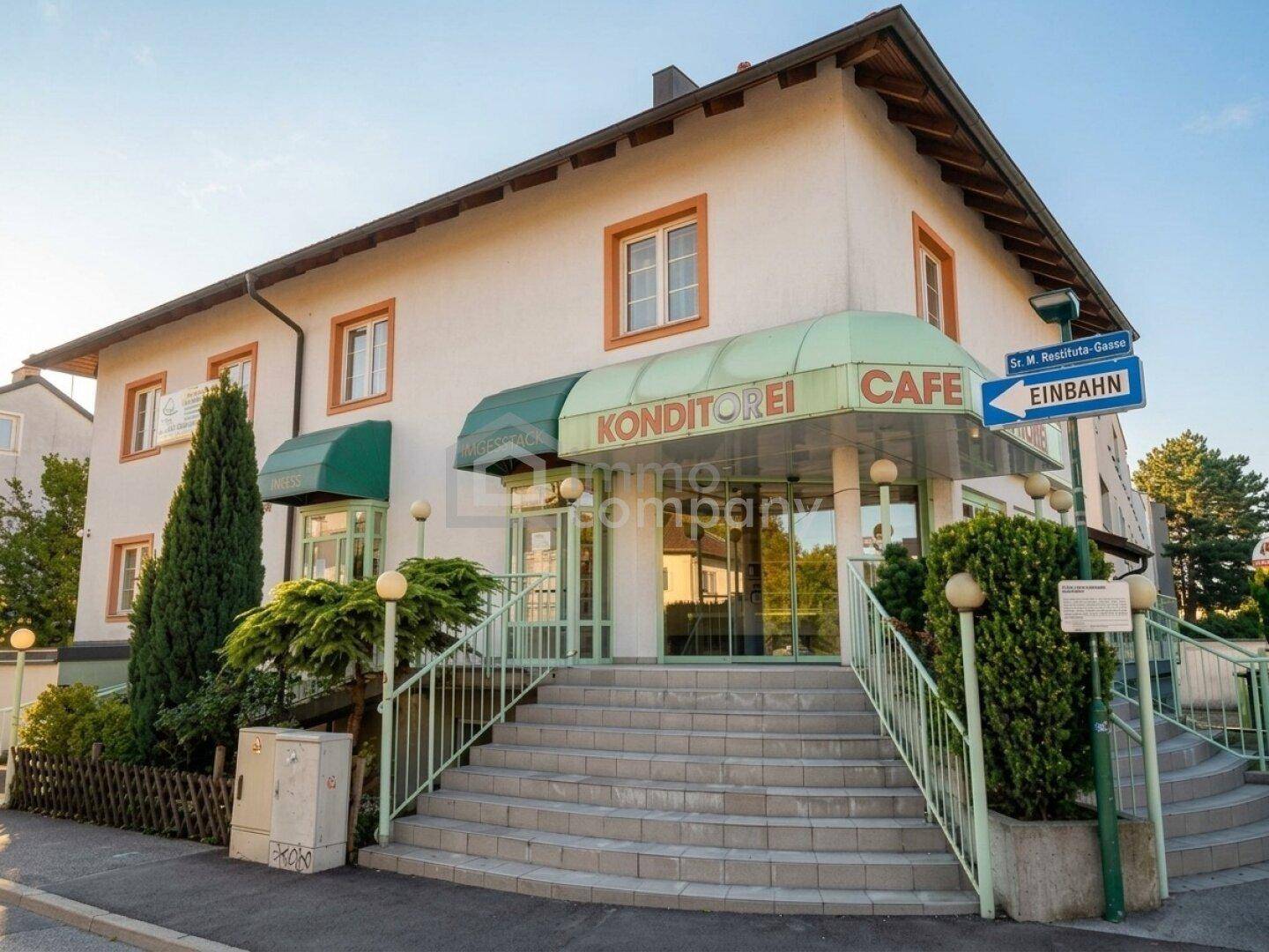 Außenansicht des Gebäudes mit Konditorei- und Café-Schildern, einladendem Eingangsbereich und Markisen.