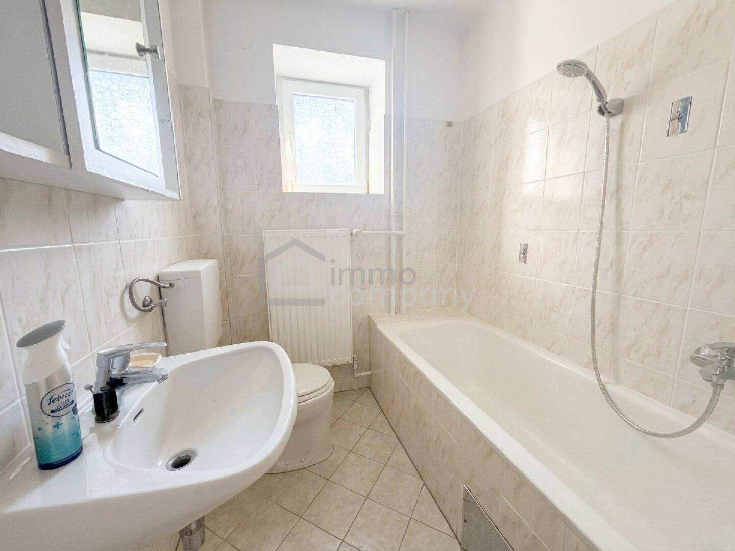 Helles Badezimmer mit Badewanne, Waschbecken und beigefarbenen Fliesen.