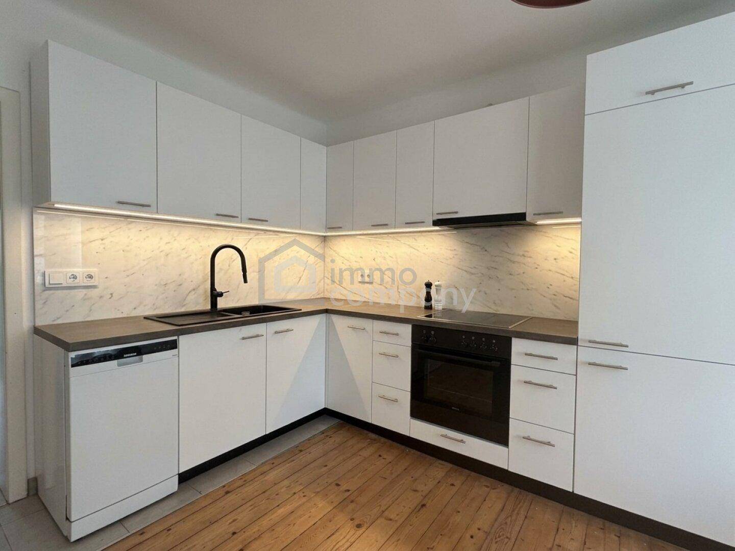 Moderne weiße Küche mit Holzfußboden, integrierten Geräten und Marmor-Rückwand.