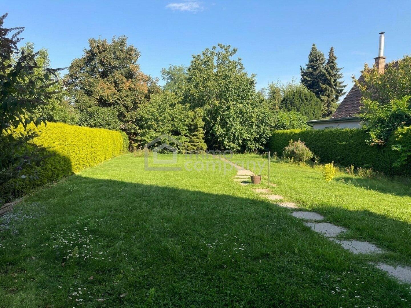 Großer, gepflegter Garten mit Rasenfläche, Hecken und einem Steinweg.