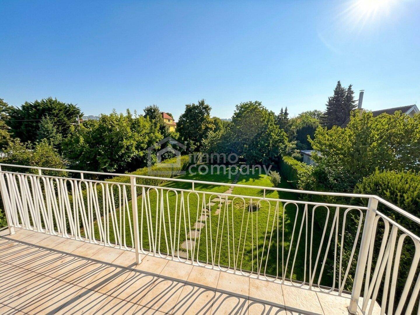 Sonniger Balkon mit Blick auf den grünen Garten und die umliegende Landschaft.