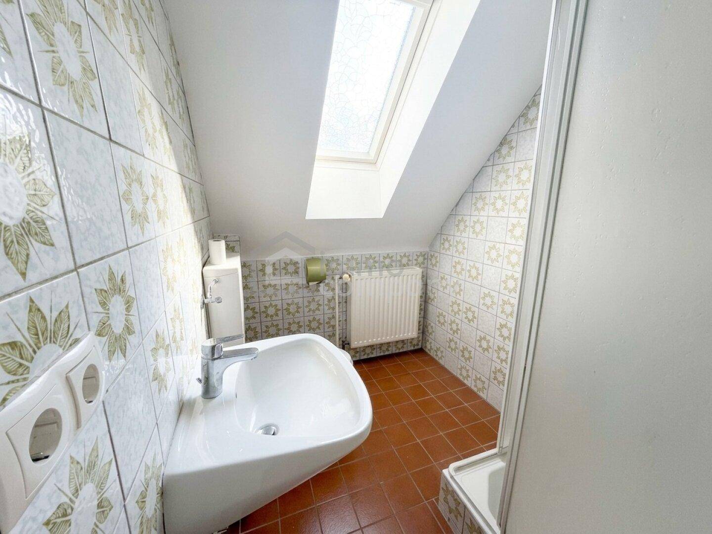 Badezimmer im Dachgeschoss mit Dachfenster, Waschbecken und Duschkabine.