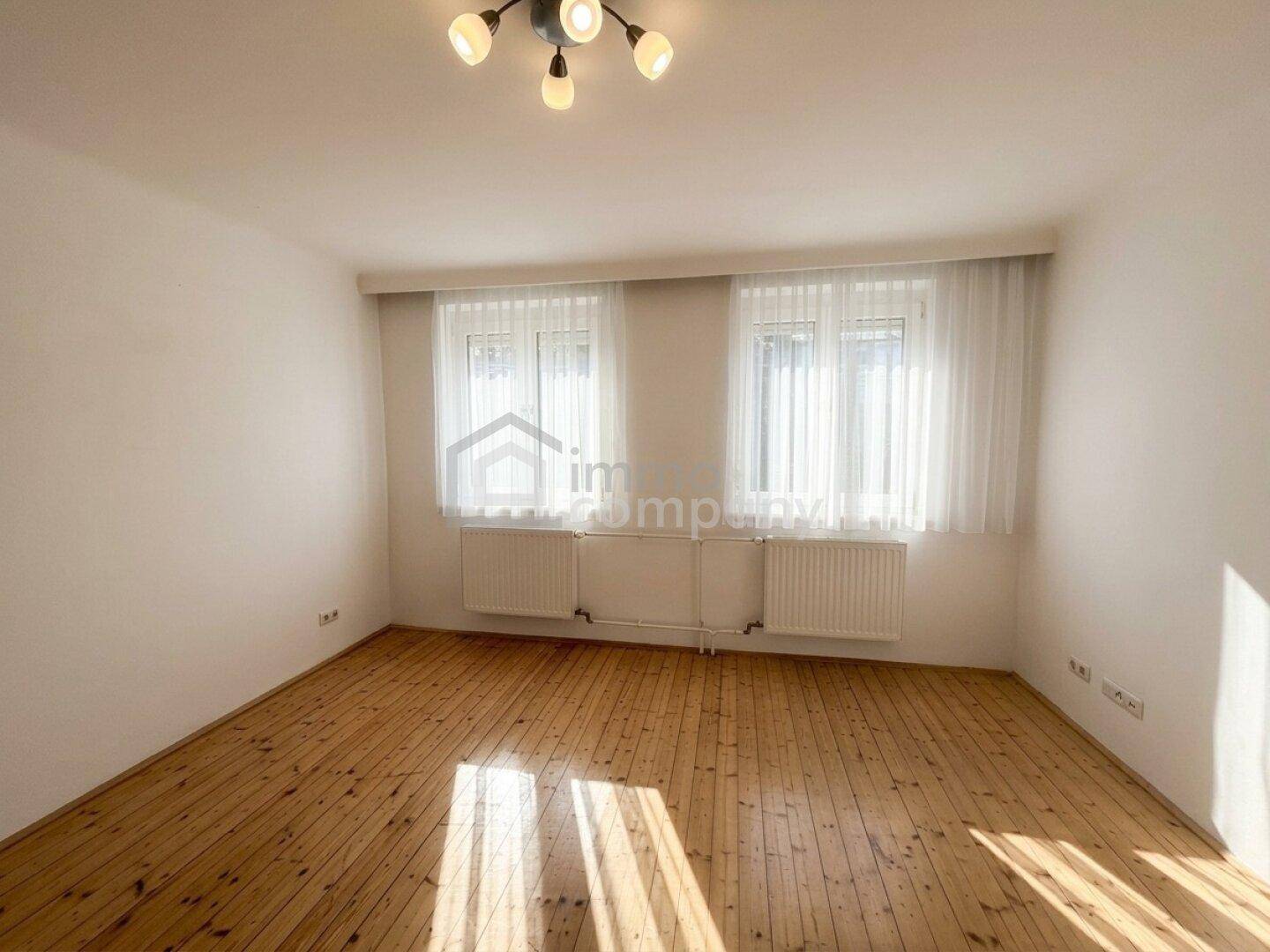 Heller Raum mit Holzfußboden und zwei Fenstern, bereit zur individuellen Gestaltung.