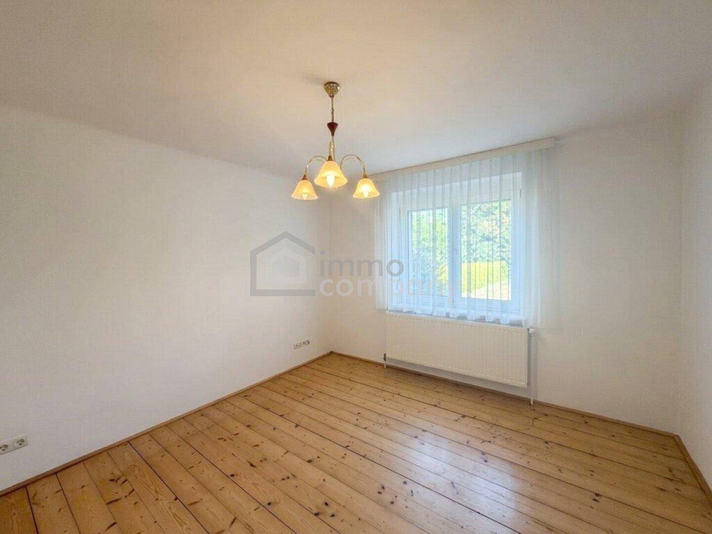 Leeres Zimmer mit Holzfußboden und einem großen Fenster, ideal als Schlaf- oder Arbeitszimmer.