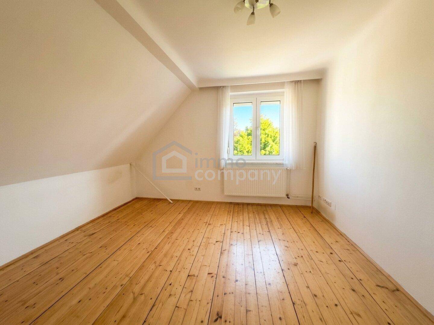 Dachgeschosszimmer mit Holzfußboden, Fenster und schrägen Wänden, ideal als Schlafzimmer.