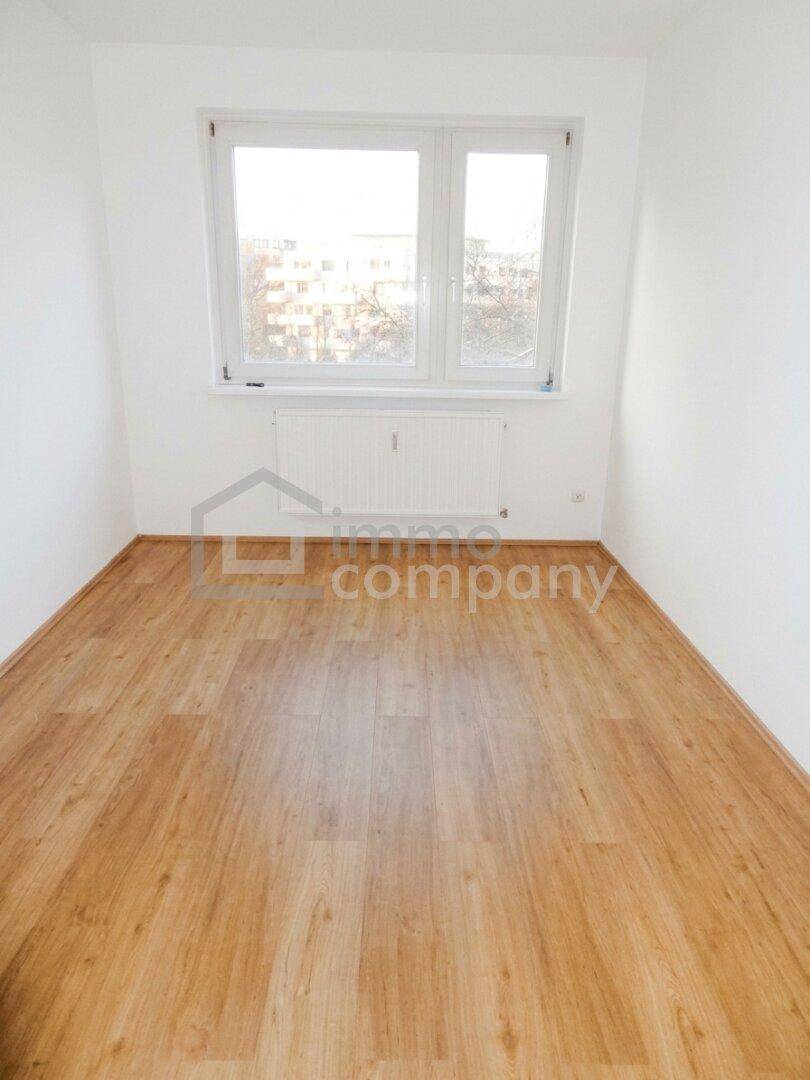 Leerer Raum mit Laminatboden und Fenster, das Tageslicht hereinlässt.