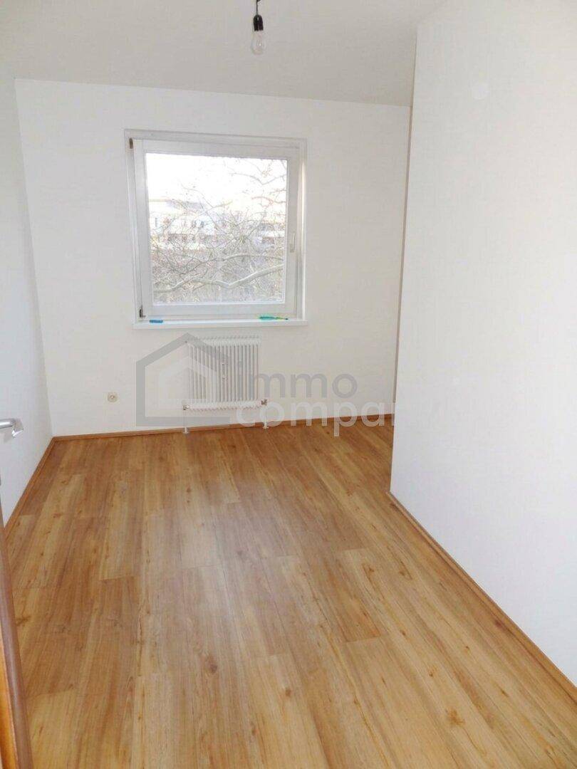 Heller, leerer Raum mit Laminatboden und einem Fenster für natürliche Belichtung.