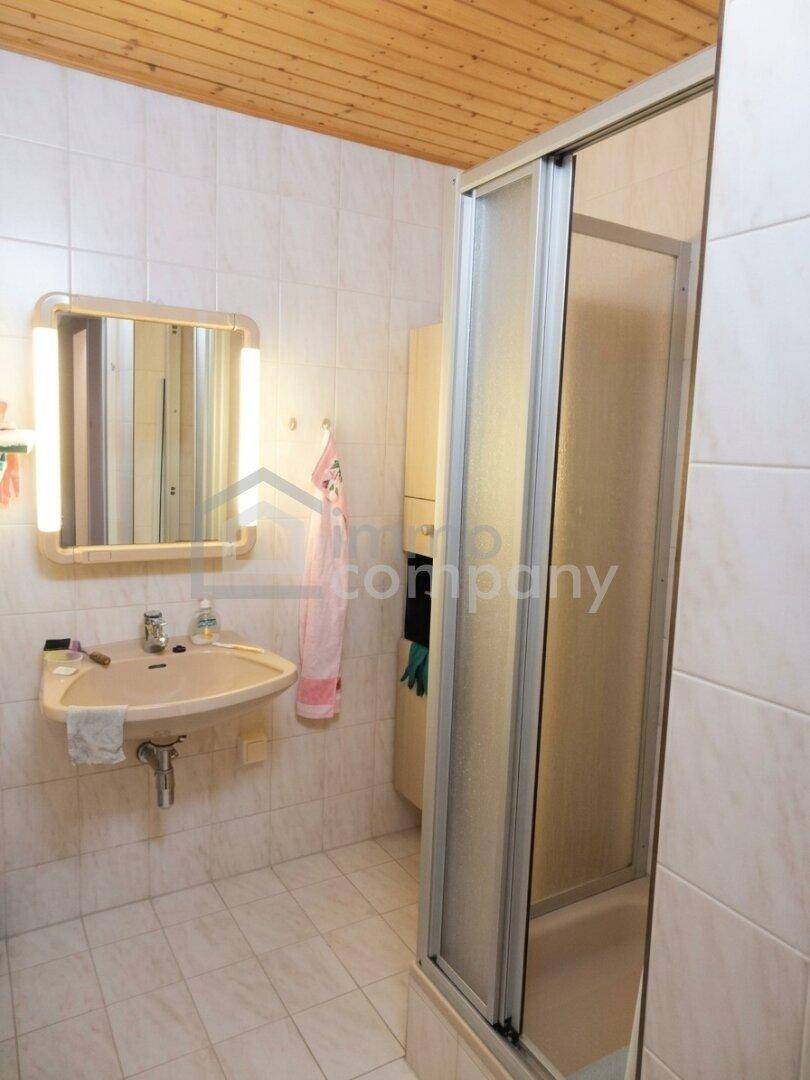 Badezimmer mit Duschkabine, Waschbecken und Spiegelschrank, gefliest und mit Holzdecke.