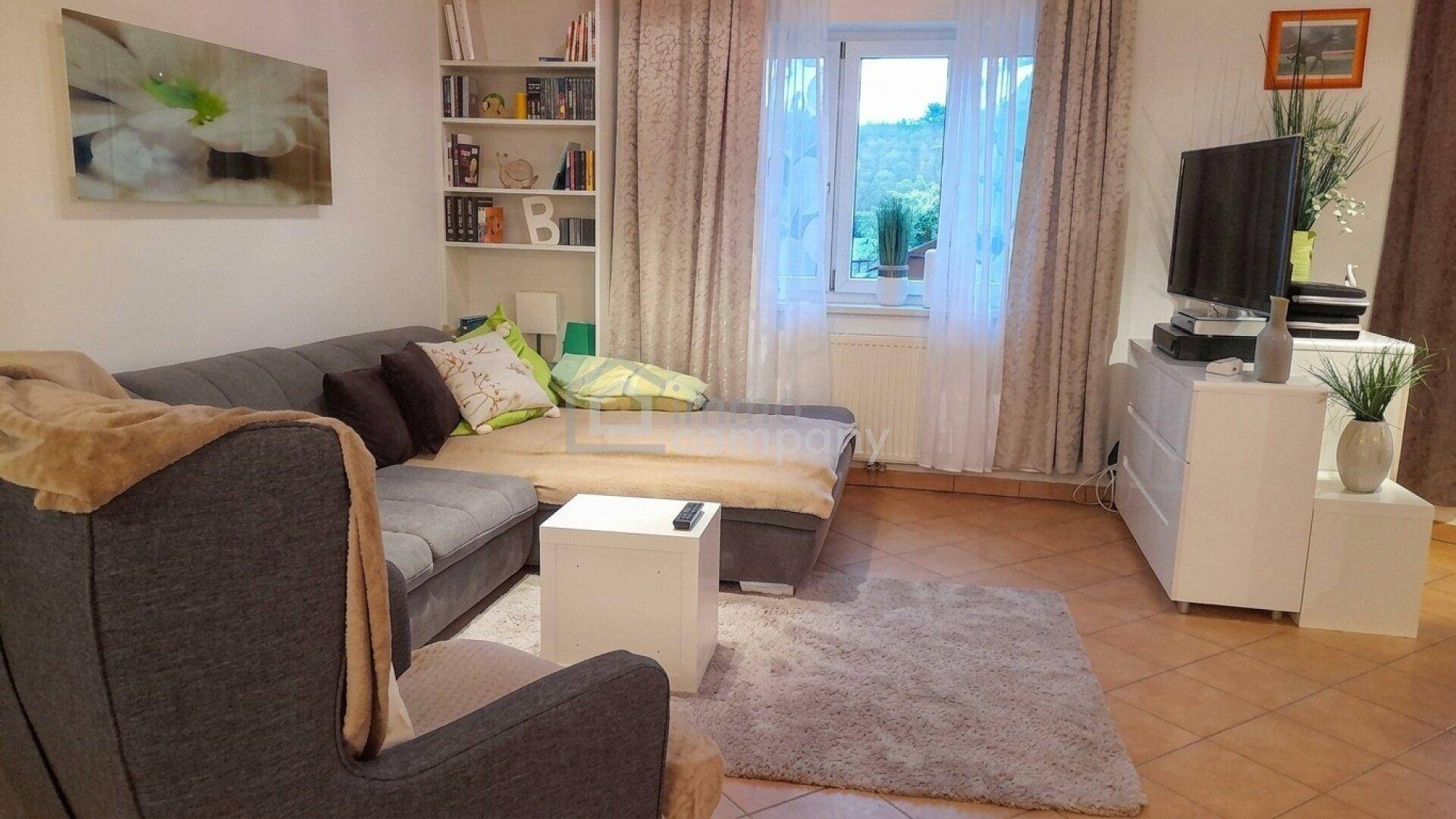 Gemütliches Wohnzimmer mit großem Sofa, Teppich, Fenster und Blick ins Grüne.