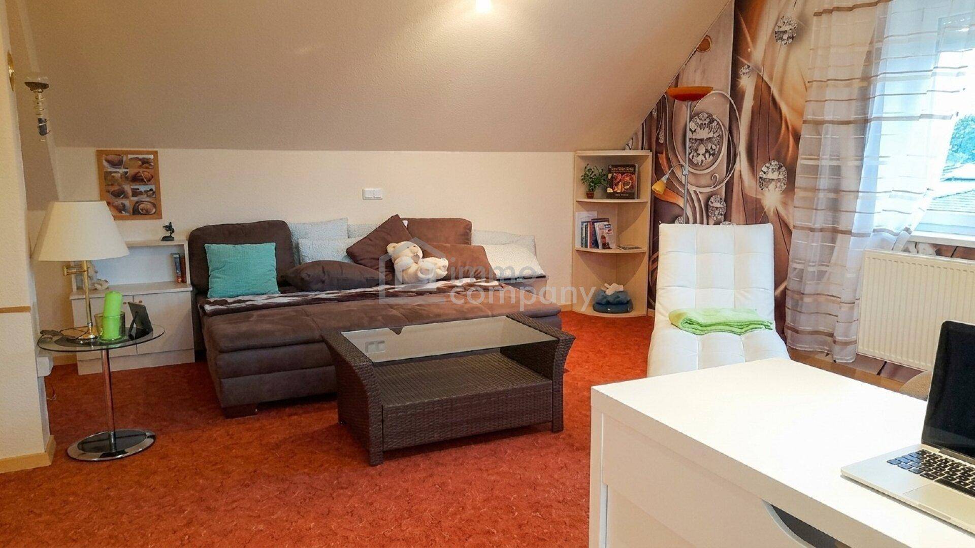 Gemütliches Dachzimmer mit Sofa, Teppichboden und schrägen Wänden.