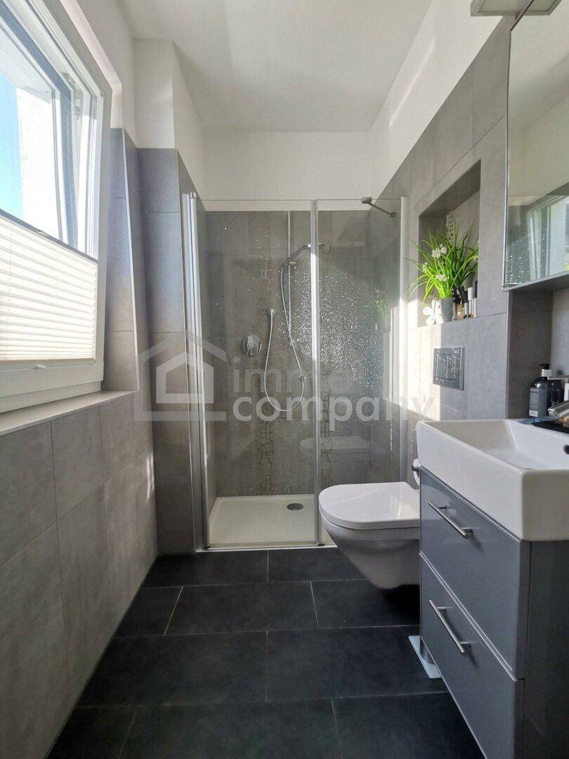 Modernes Badezimmer mit Duschkabine, WC, Einzelwaschbecken und grauen Fliesen.