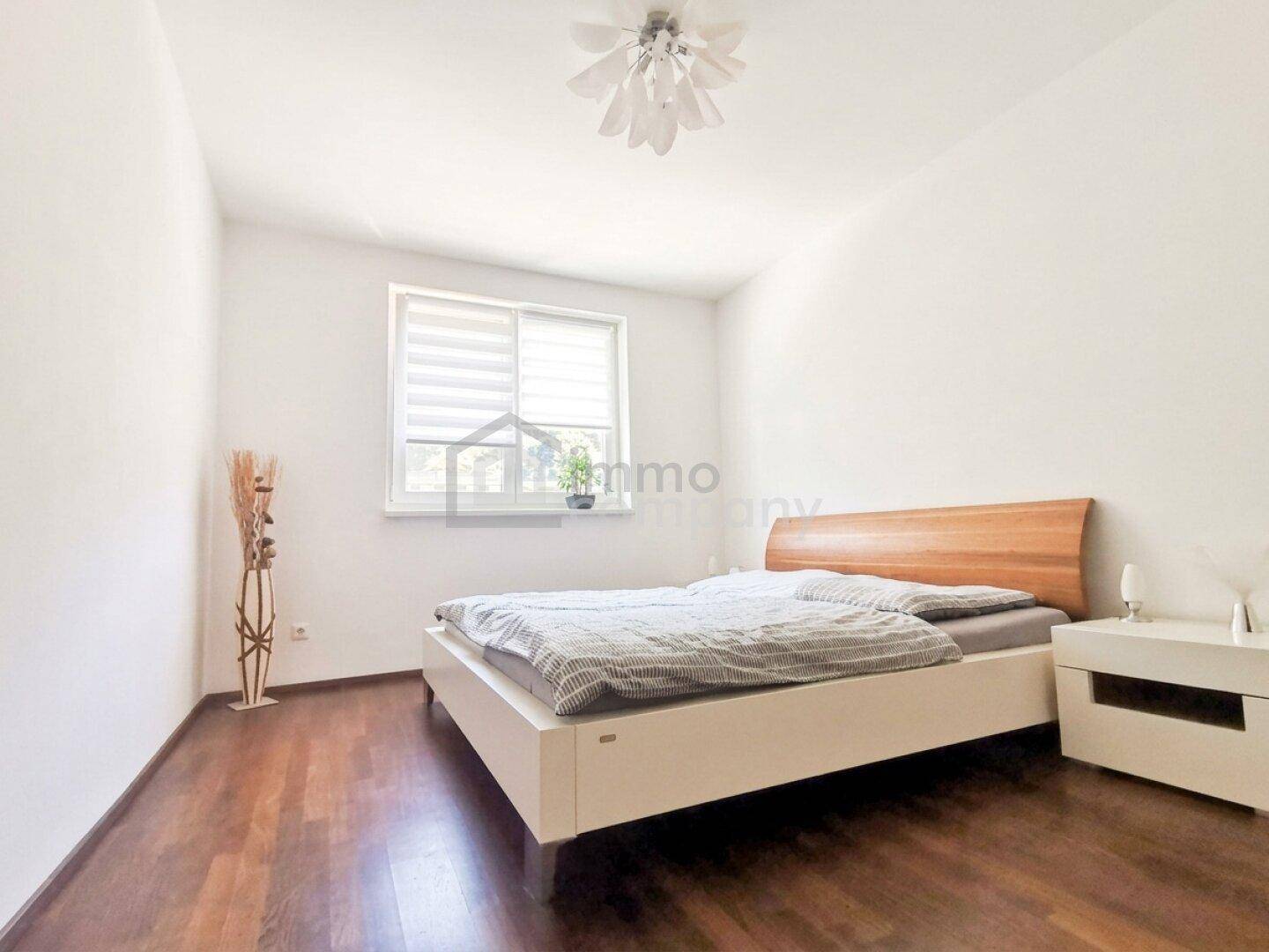 Ruhiges Schlafzimmer mit Doppelbett, Nachttisch und Fenster mit Jalousien.
