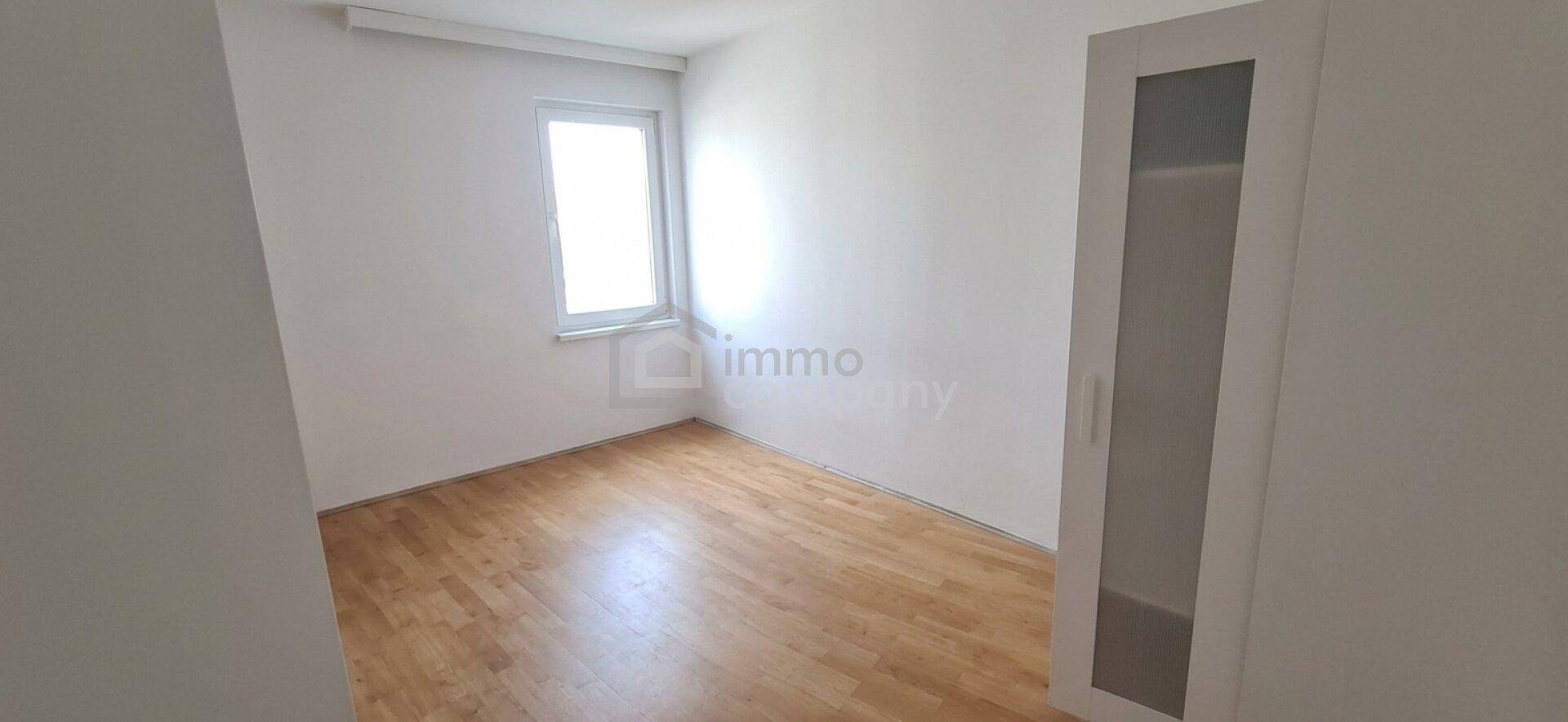 Helles Schlafzimmer mit hellem Holzfußboden, weißen Wänden und einem Fenster.