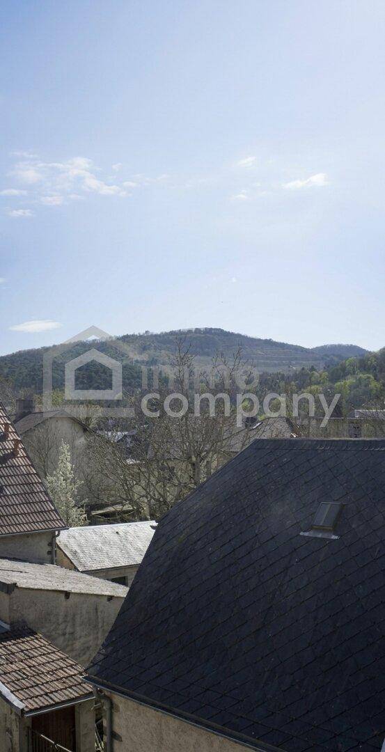 Weitblick über Dächer auf eine grüne Berglandschaft unter blauem Himmel.