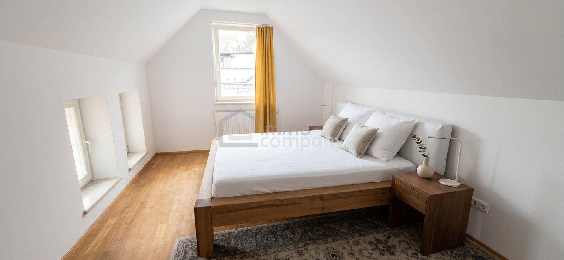 Gemütliches Schlafzimmer im Dachgeschoss mit schrägen Decken, Holzbett und Fenster.