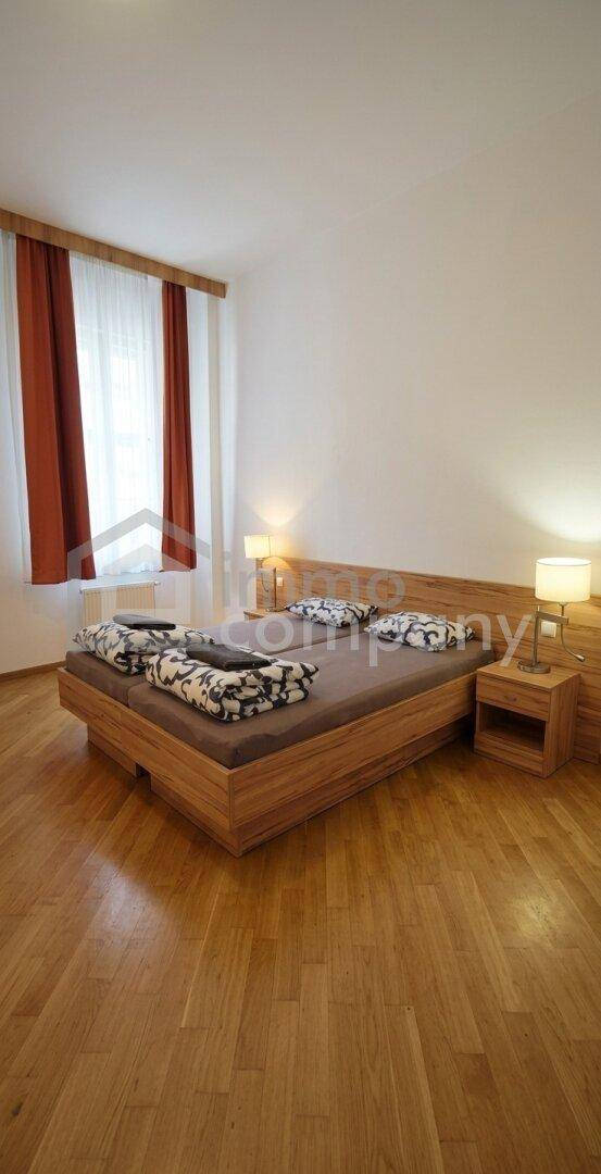 Gemütliches Schlafzimmer mit Holzbett, Nachttischen, Lampen und Fenster mit roten Vorhängen.
