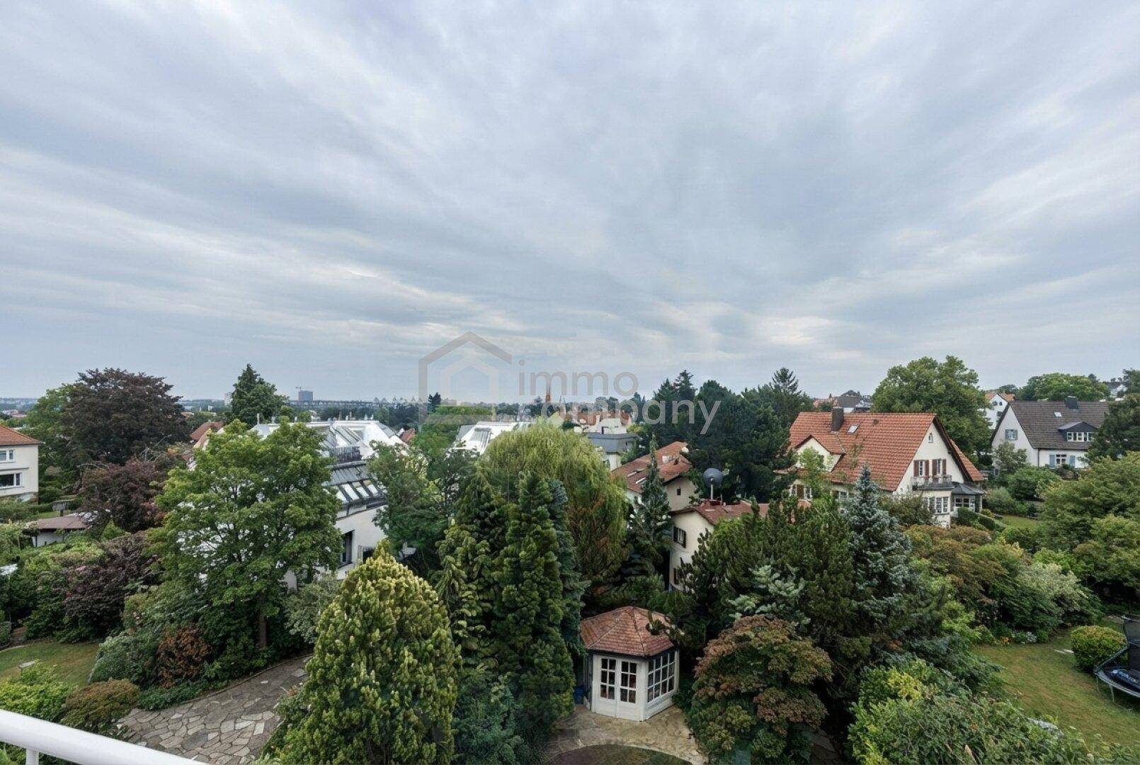 Weitläufiger Blick über eine grüne Wohngegend mit vielen Bäumen und Einfamilienhäusern unter bewölktem Himmel.