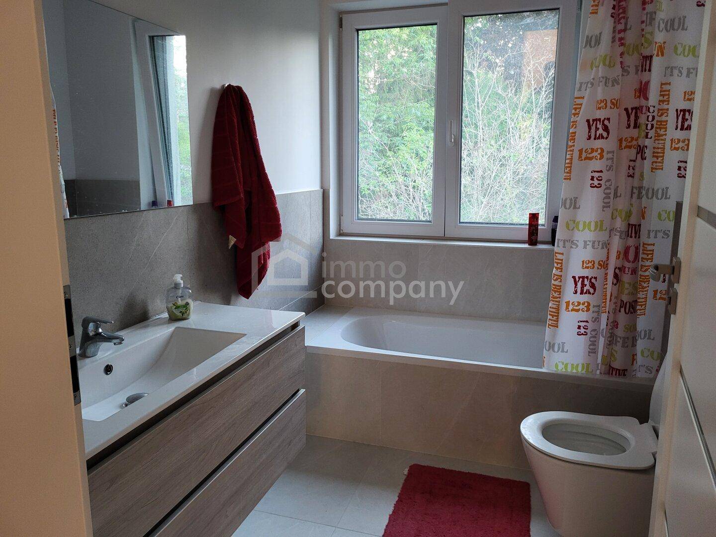 Modernes Badezimmer mit Badewanne, Einzelwaschbecken und Fenster, ausgestattet mit hellen Fliesen.
