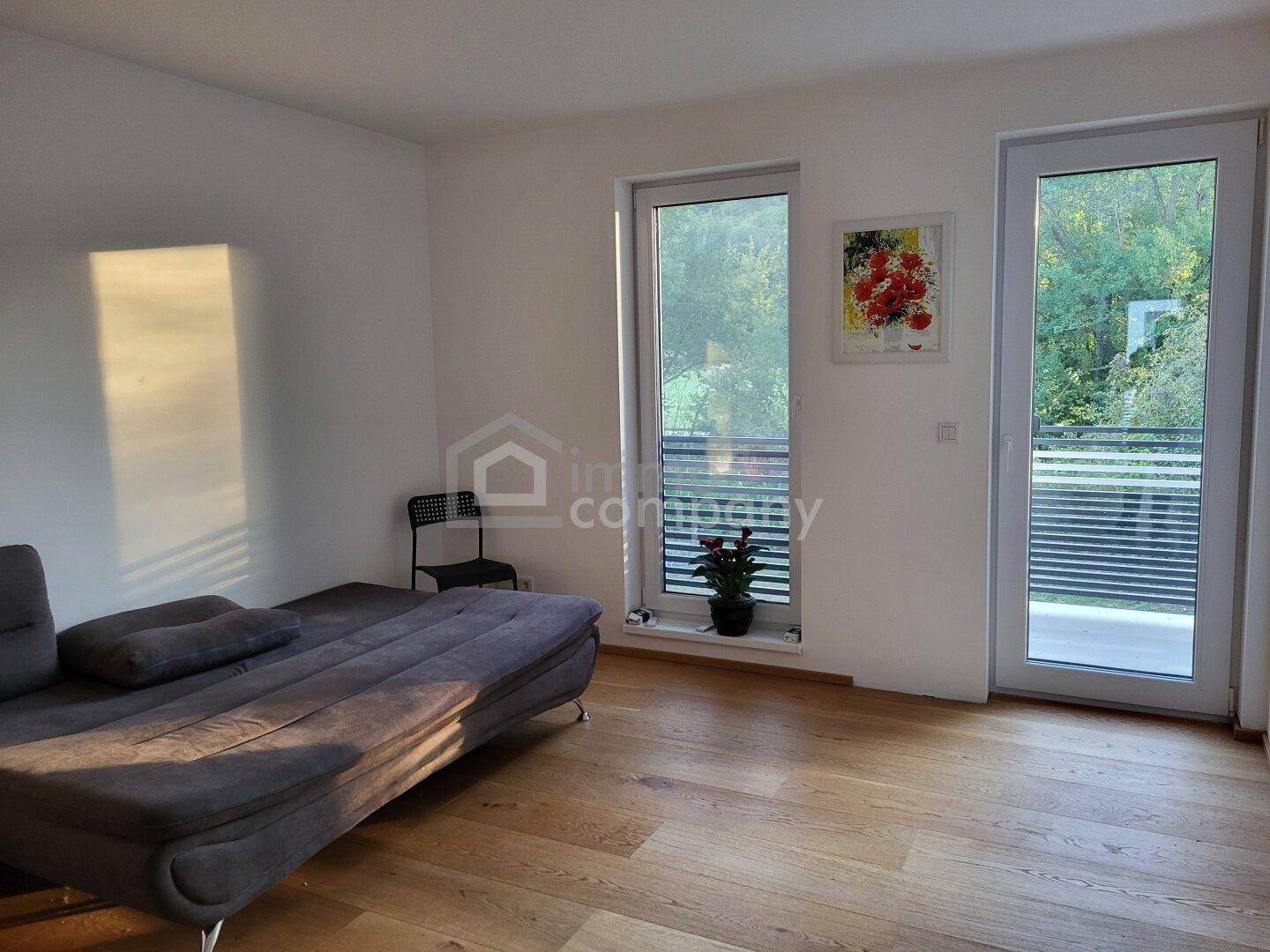 Helles Wohnzimmer mit Holzboden, Sofa und Zugang zu einem Balkon oder einer Terrasse.