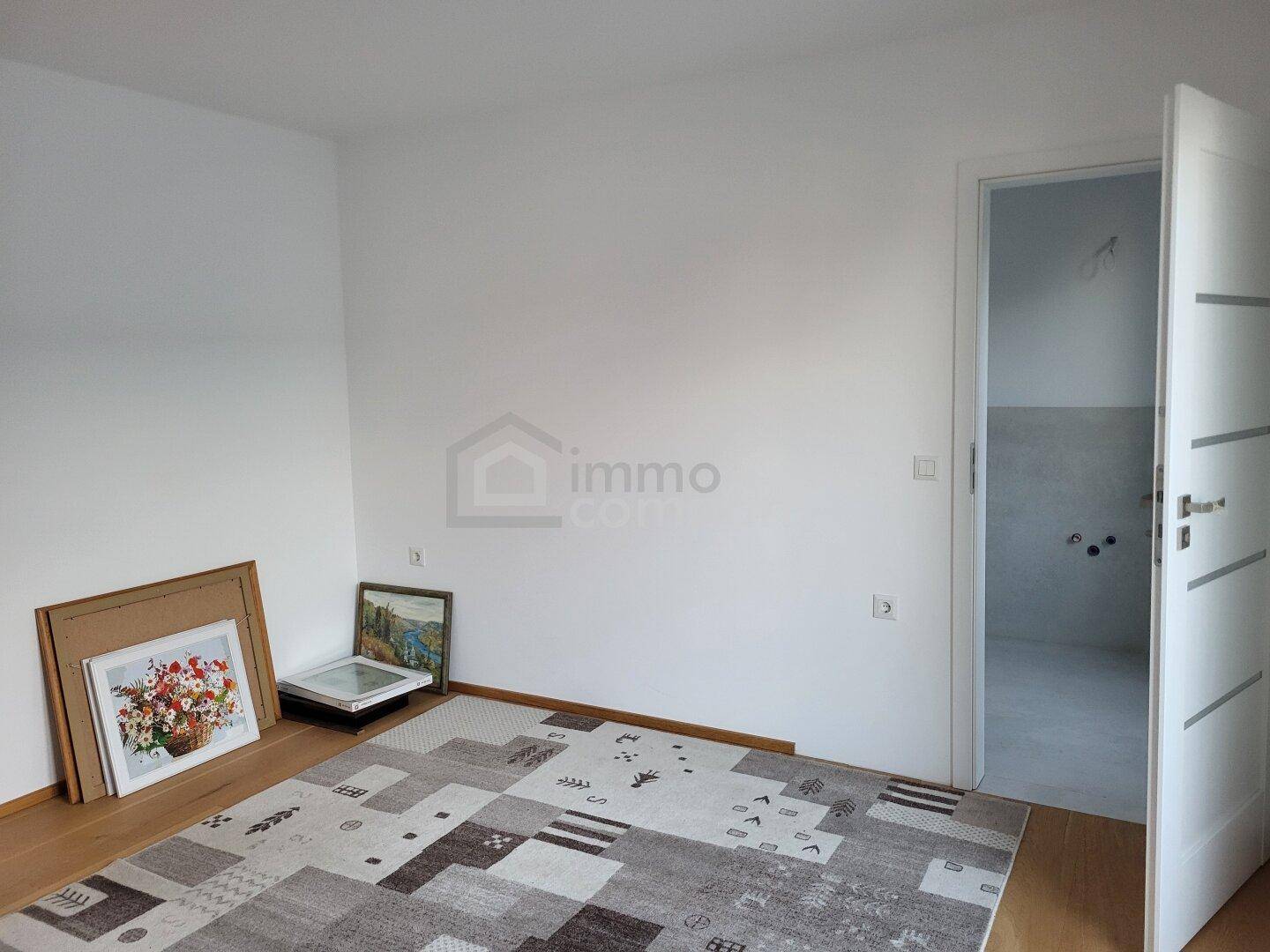 Helles Schlafzimmer mit Holzboden und einem Teppich, angrenzend an ein Badezimmer mit offener Tür.