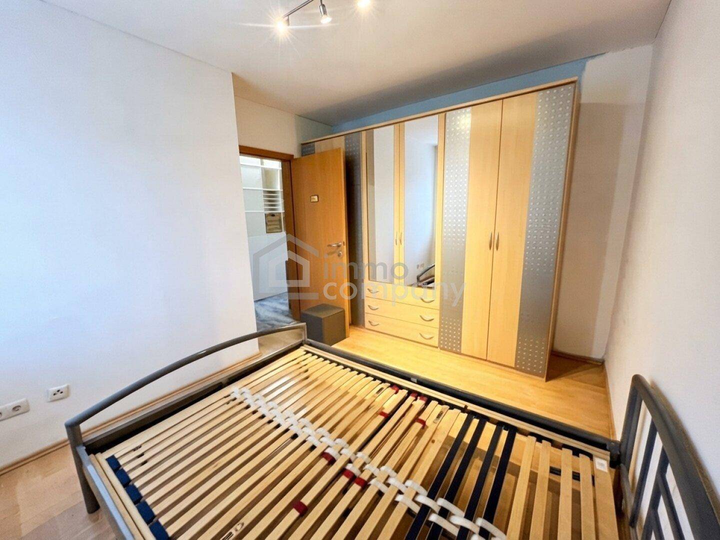 Schlafzimmer mit Holzboden, Bettrahmen und großem Einbauschrank mit Spiegeltüren.