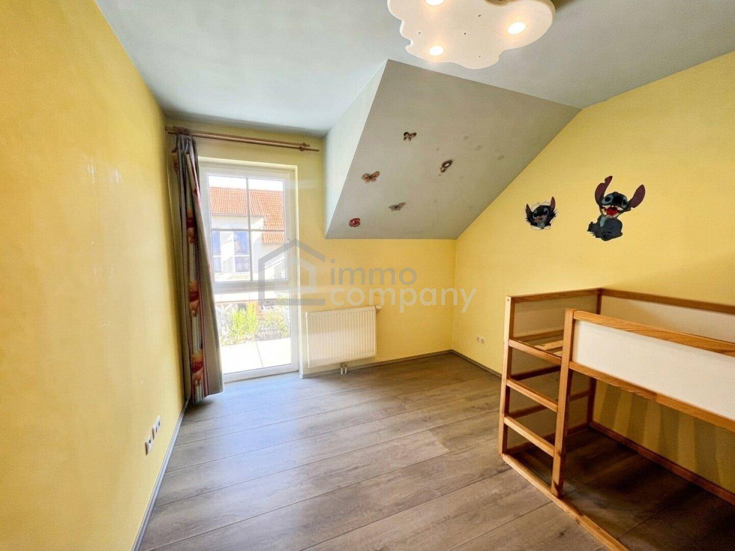 Kinderzimmer mit gelben Wänden, Laminatboden, Dachschräge und Zugang zu einem Außenbereich.