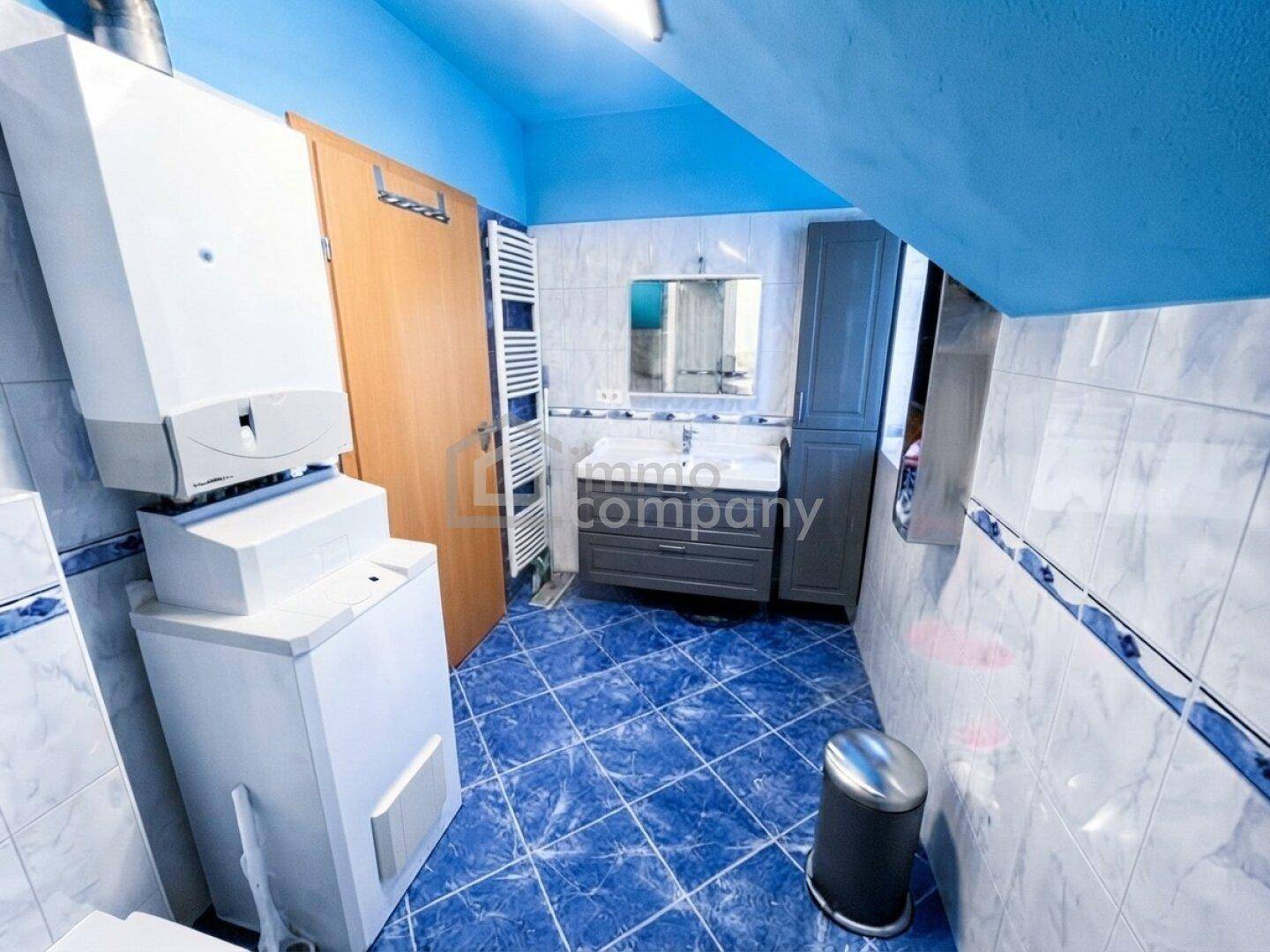 Badezimmer im Dachgeschoss mit blauen Fliesen, Waschbecken und Heizungsanlage.