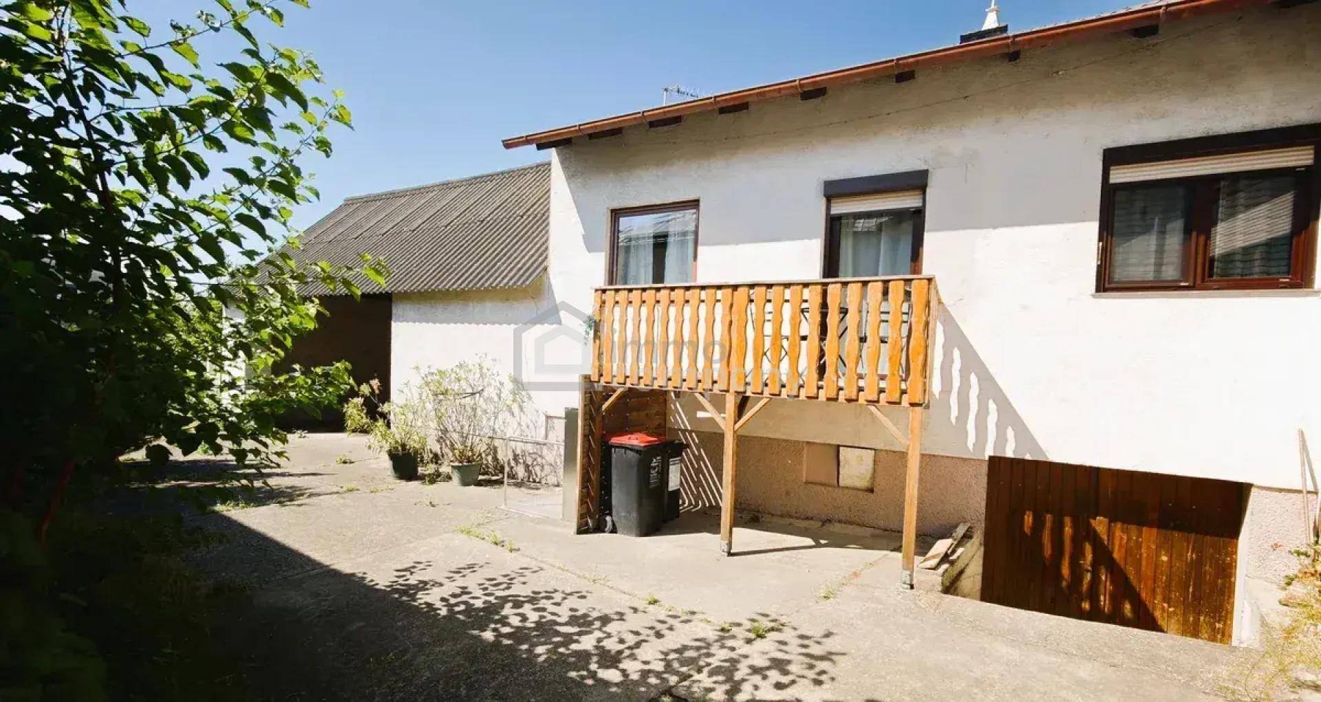 Außenansicht des Hauses mit kleinem Holzbalkon und einem gepflasterten Hofbereich.