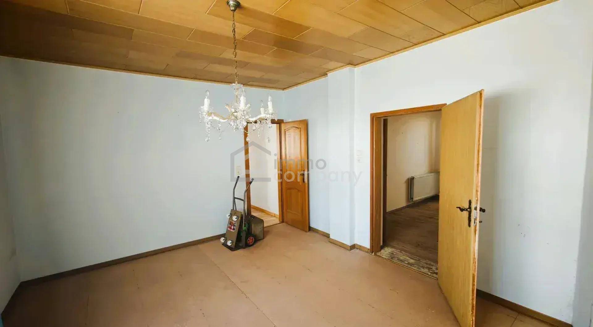 Leerer Raum mit Holzdecke und Kronleuchter, bereit für neue Bodenbeläge und Nutzung.