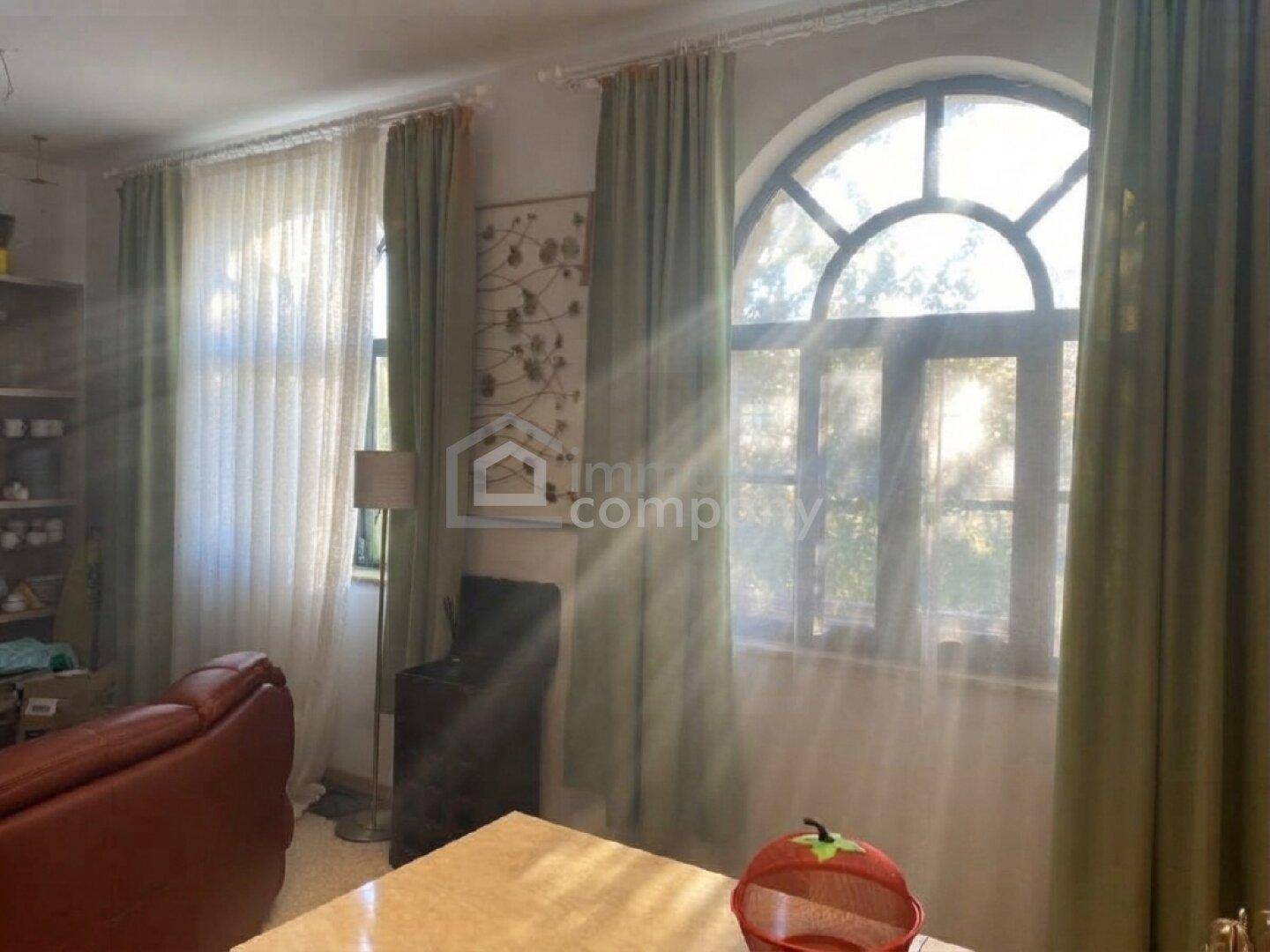 Lichtdurchflutetes Wohnzimmer mit großen Bogenfenstern und Vorhängen, die viel Tageslicht hereinlassen.