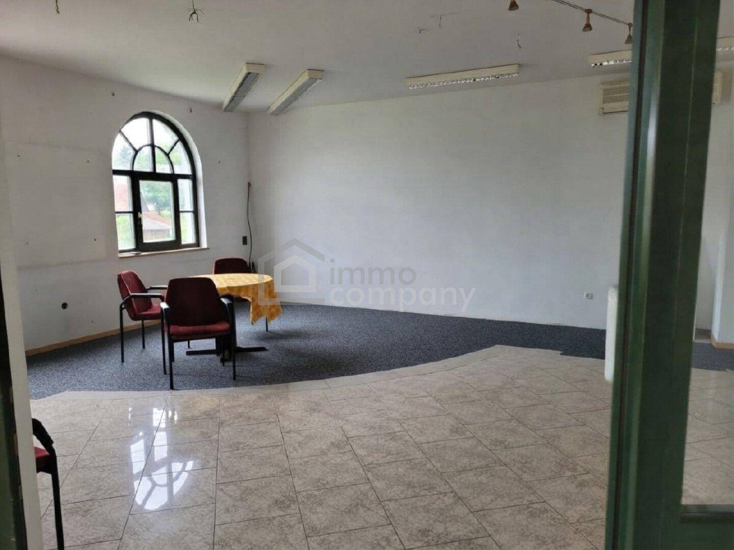 Geräumiger Raum mit Fliesen- und Teppichboden, einem Bogenfenster und kleiner Sitzecke.