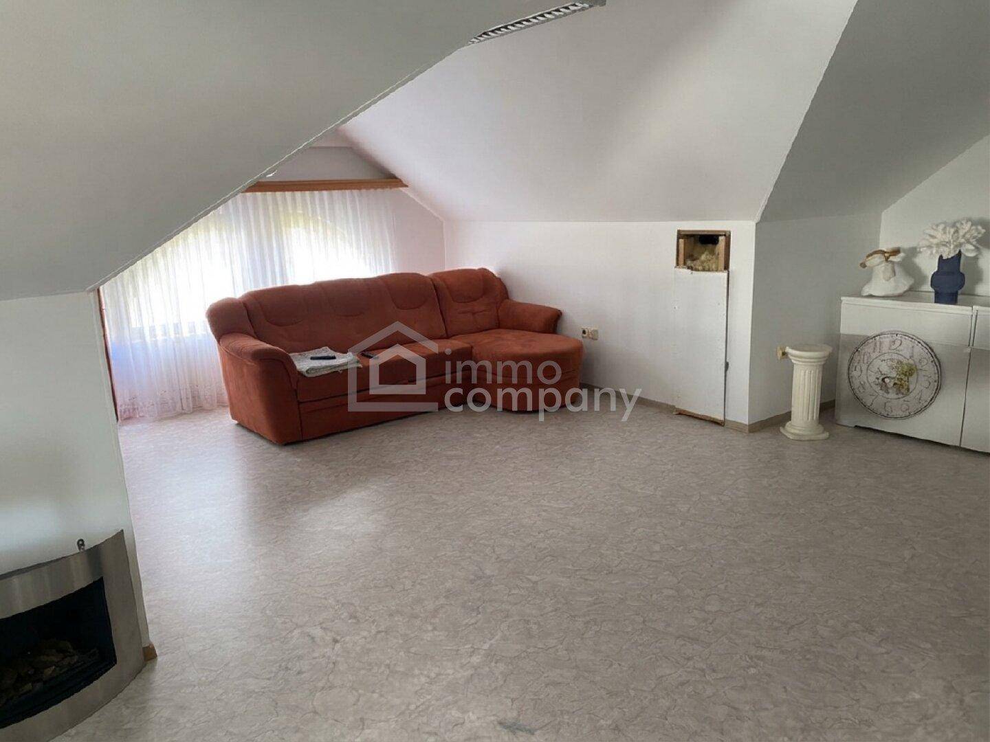Gemütliches Wohnzimmer im Dachgeschoss mit Schrägen, Sofa und Kamin.