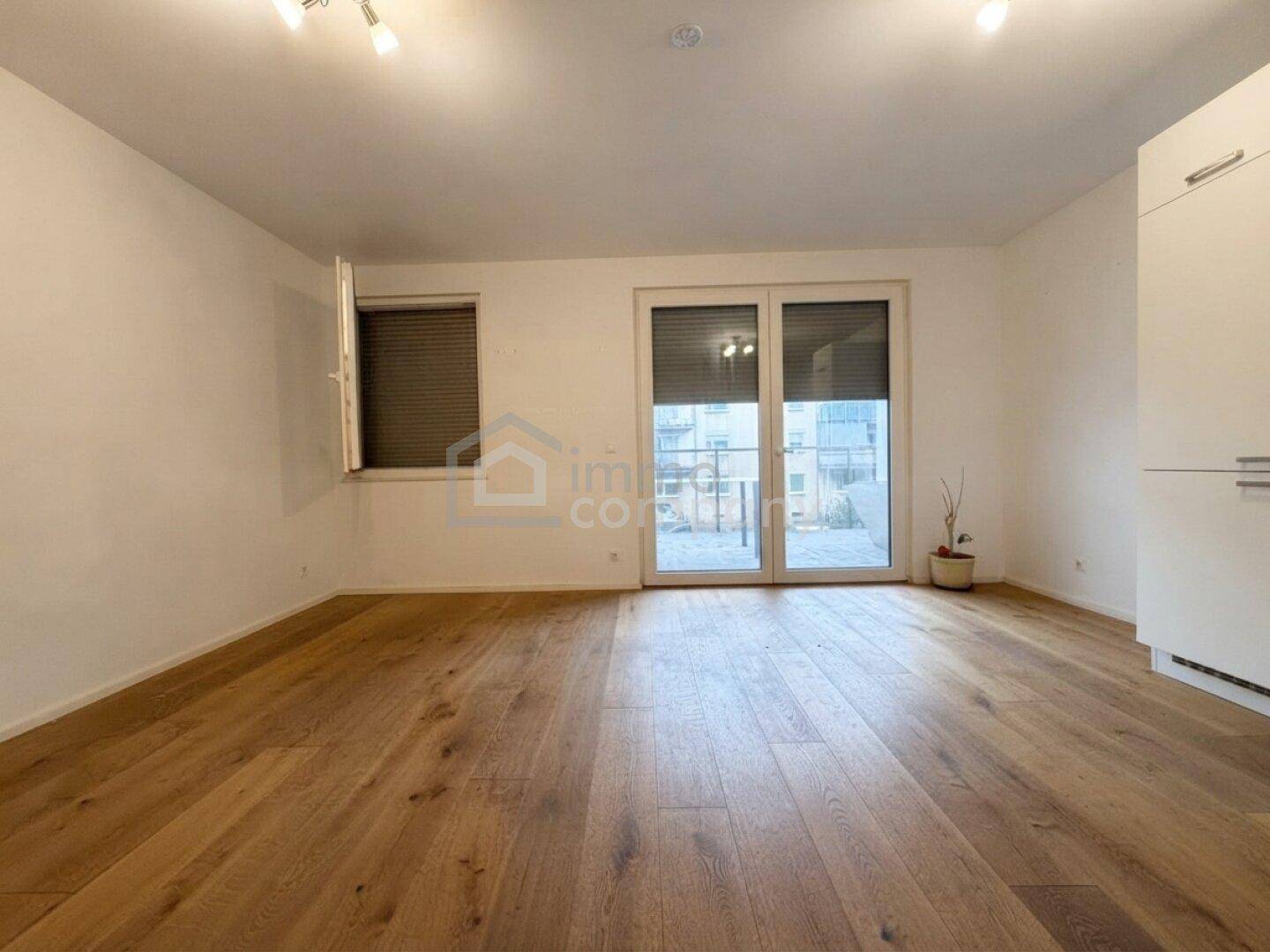 Geräumiges Wohnzimmer mit Holzboden und großen Fenstern, die viel Tageslicht hereinlassen.