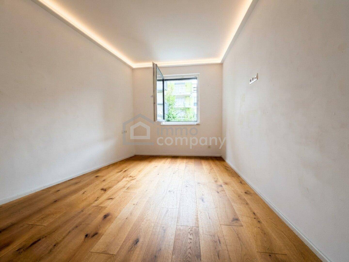 Leeres Schlafzimmer mit Holzboden und einem Fenster, das den Raum hell erscheinen lässt.