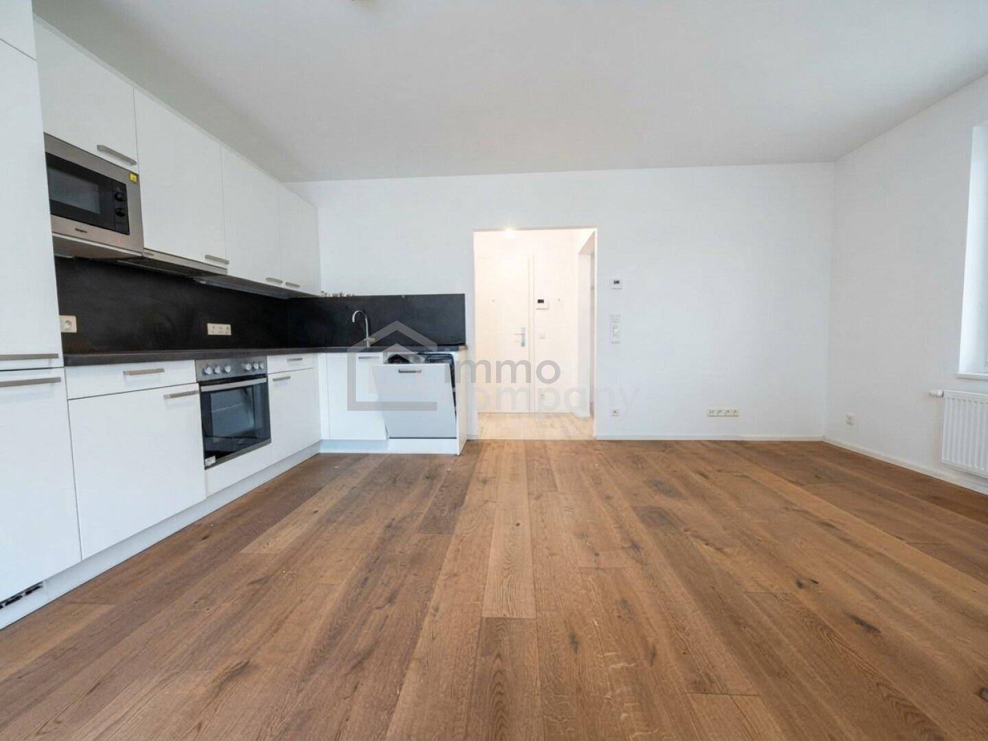 Heller offener Wohnbereich mit moderner Einbauküche und hochwertigem Holzboden.