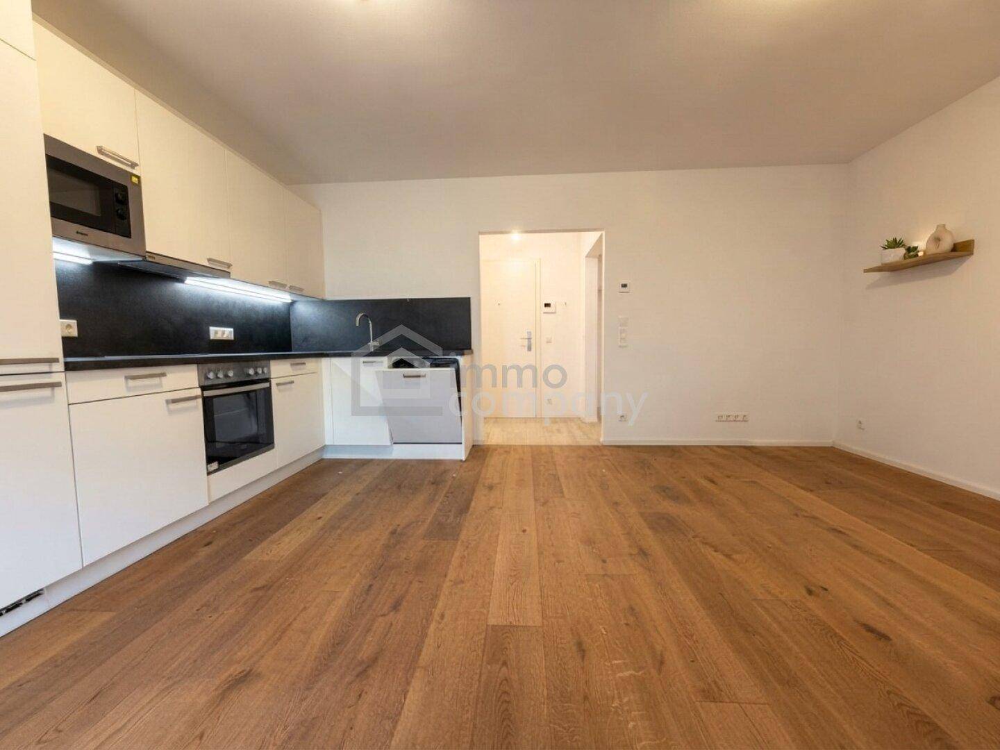 Leere offene Küche mit weißen Einbauschränken und Holzboden, bereit zur Einrichtung.
