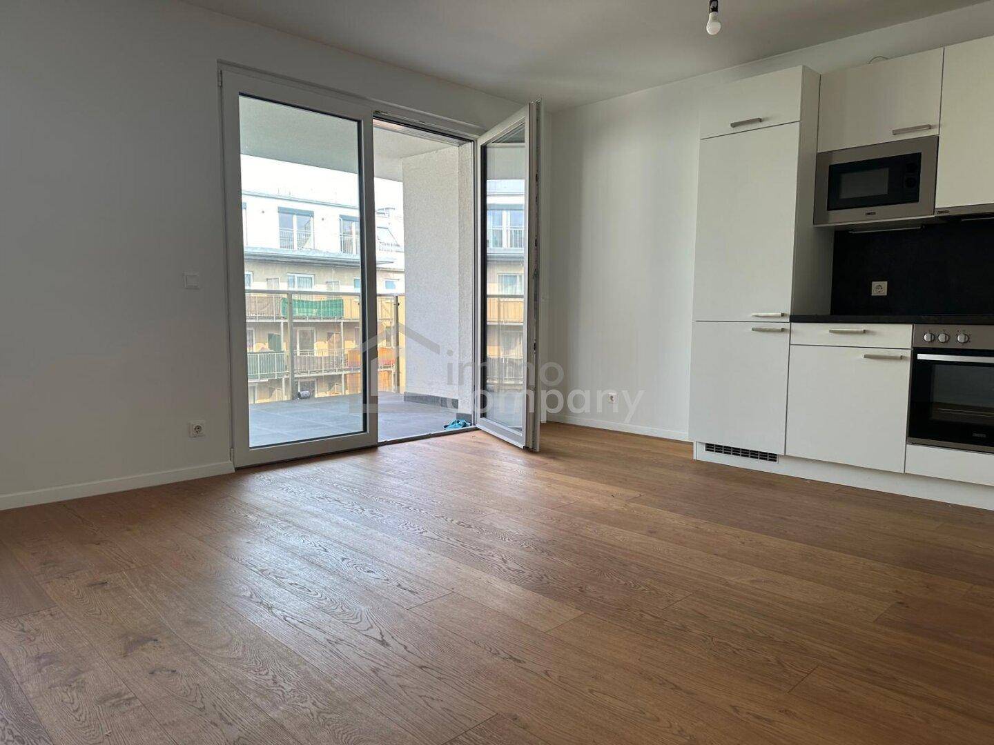 Geräumiger, leerer Wohnbereich mit offener Küche und direktem Zugang zum Balkon.