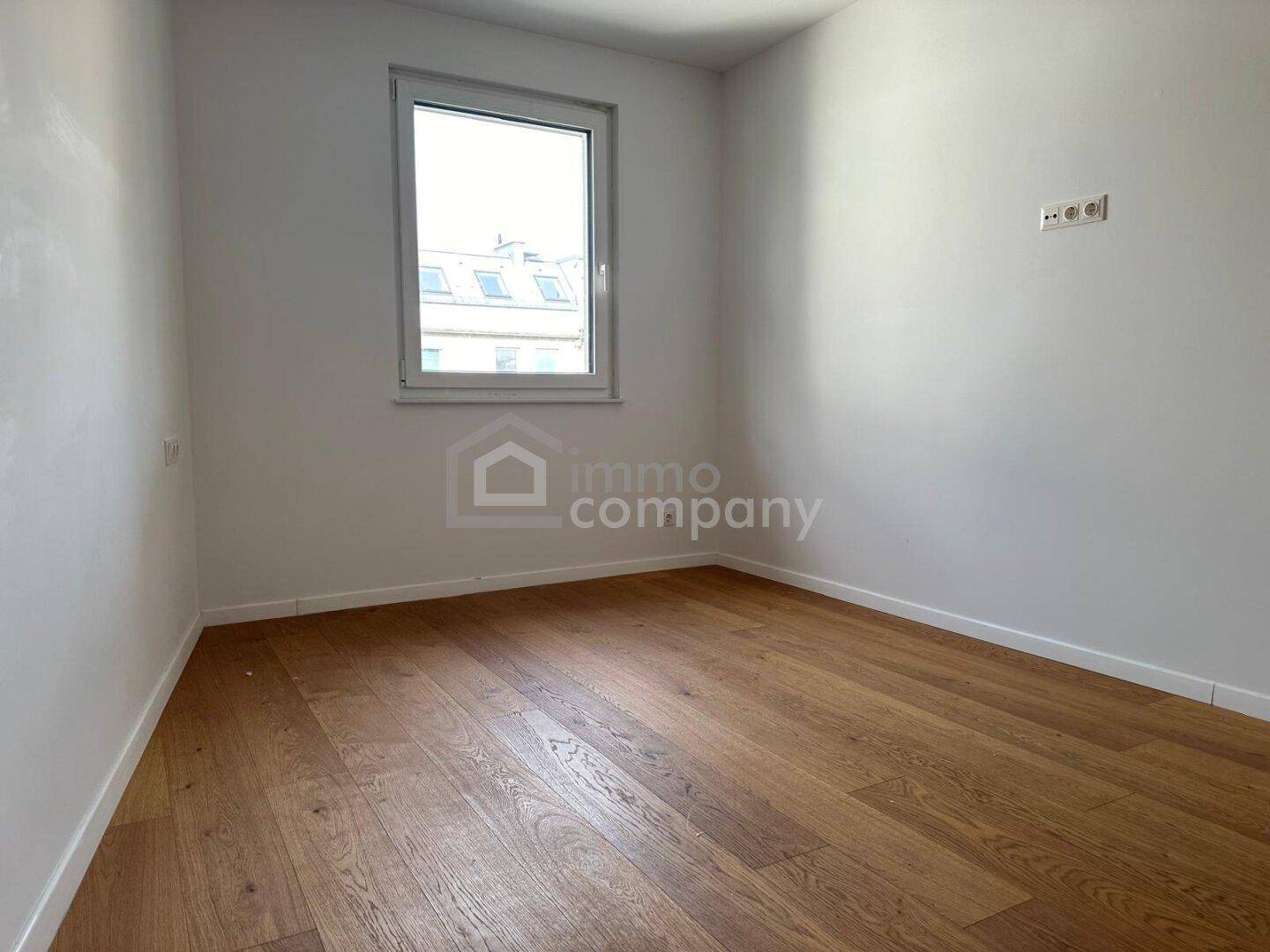 Helles, leeres Schlafzimmer mit Holzboden und einem großen Fenster.