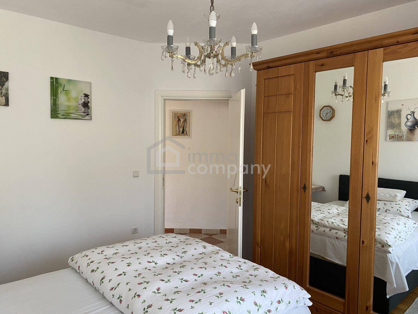 Helles Schlafzimmer mit Einzelbett, Holzschrank und einem Kronleuchter an der Decke.