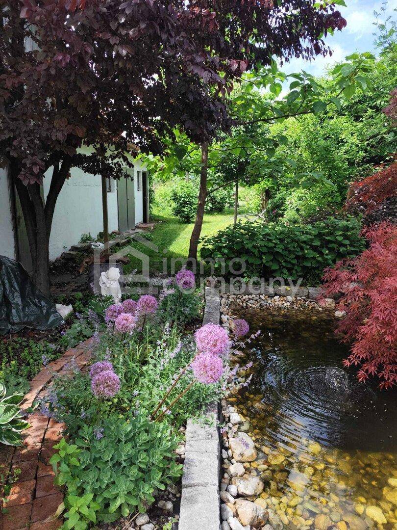 Üppiger Garten mit Teich, blühenden Blumen und vielfältiger Bepflanzung neben dem Gebäude.