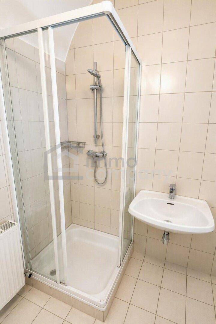 Badezimmer mit Duschkabine und Waschbecken, ausgestattet mit hellen Fliesen und Heizkörper.