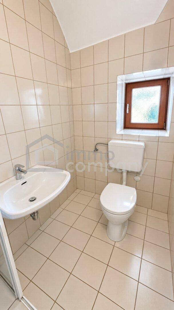 Helles Badezimmer mit WC, Waschbecken und Fenster, komplett gefliest für einfache Pflege.