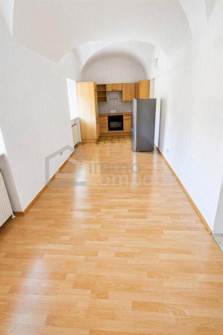 Offene Küche mit Holzschränken, Backofen und Kühlschrank, integriert in einen Raum mit Gewölbedecke.