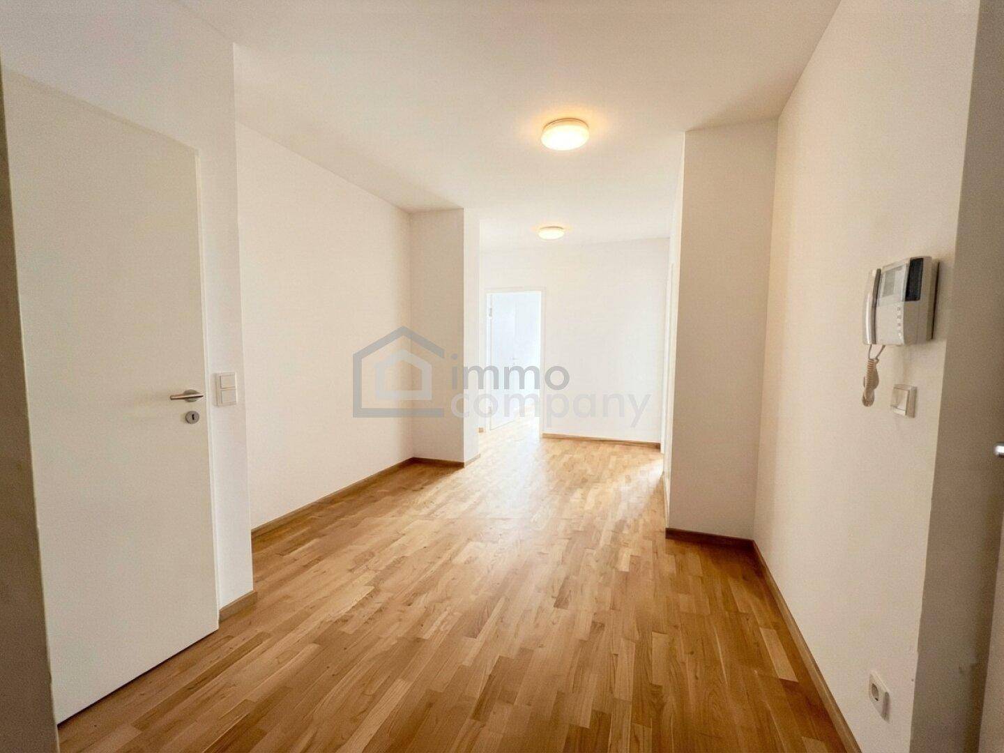 Langer, heller Flur mit Parkettboden und weiß gestrichenen Wänden, ausgestattet mit einer Gegensprechanlage.