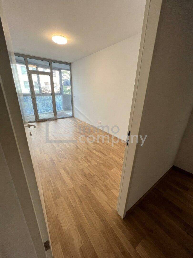 Leeres Schlafzimmer mit Holzboden und großen Fenstern, die viel Tageslicht hereinlassen.