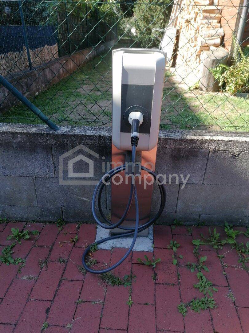 Ladestation für Elektrofahrzeuge im Außenbereich, auf Ziegelpflaster neben einem Zaun.